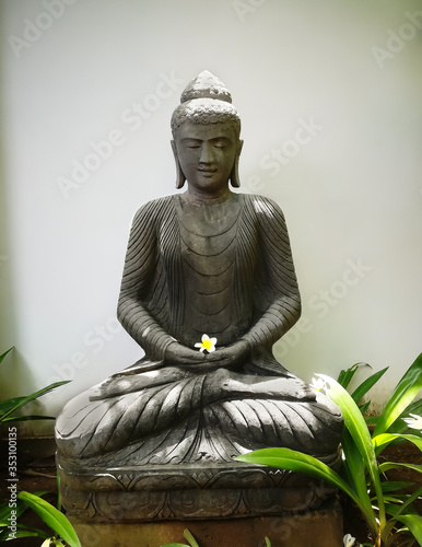 statue of Buddha in a garden holding a plumeria flower