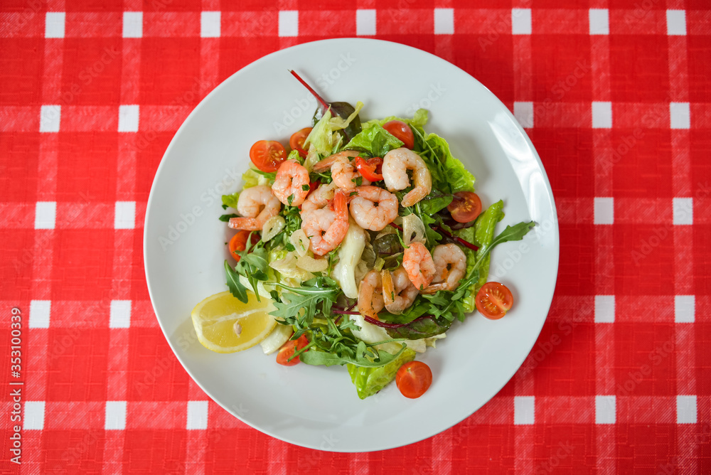 Vegetable salad with shrimp on white plate on red-white tablecloth Vegetable salad with shrimp on white plate on red-white tablecloth
