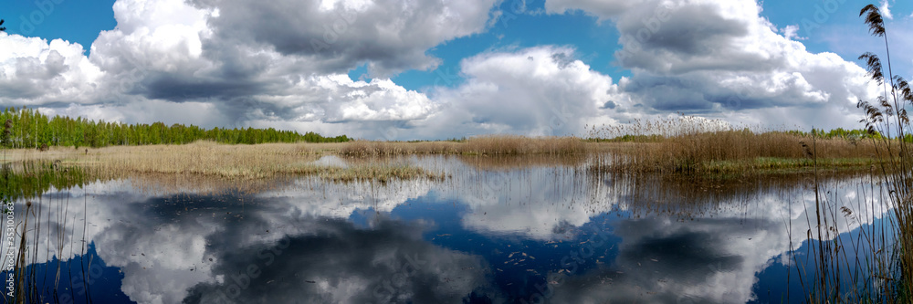 Panoramic view of a calm lake with white cumulus clouds