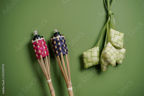 Top view of ketupat or rice dumpling with  bamboo torches isolated over green background. Hari Raya festival concept. photo