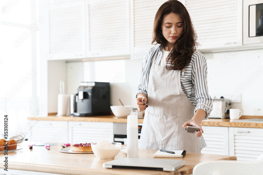 Image of focused brunette woman using cellphone while cooking pie Image of focused brunette woman using cellphone while cooking pie