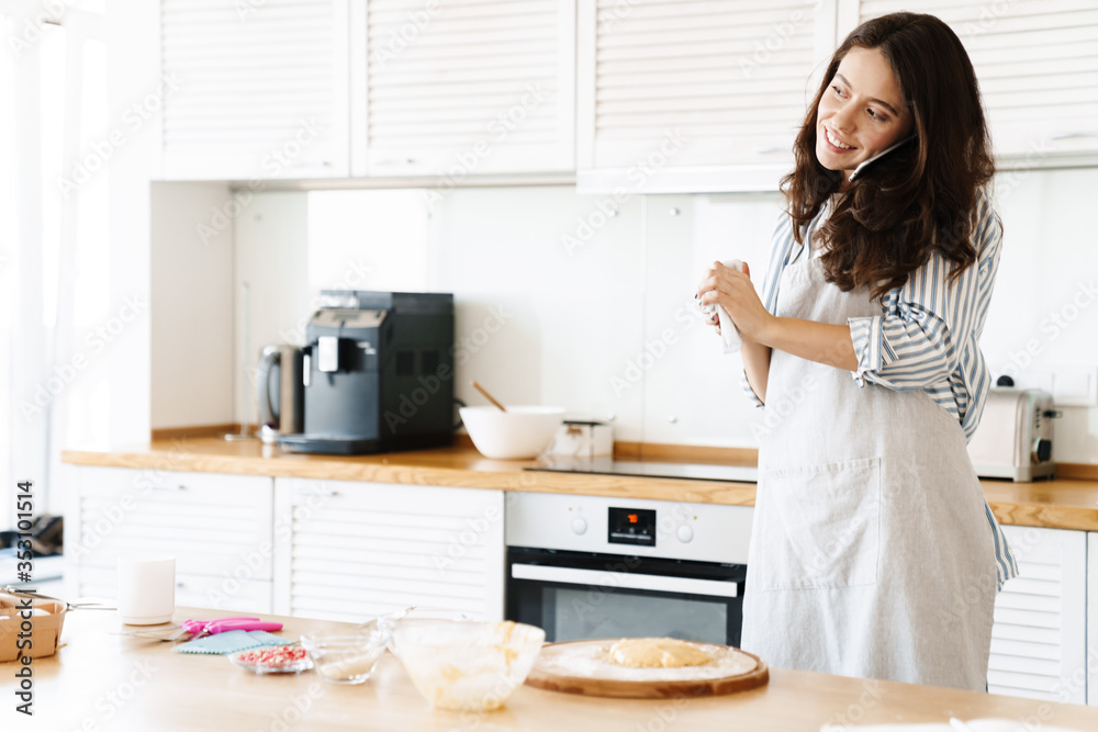 Image of laughing woman talking on cellphone while cooking pie Image of laughing woman talking on cellphone while cooking pie