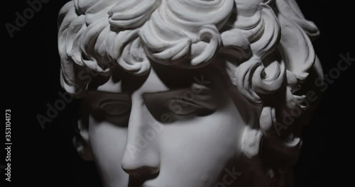 Epic studio close-up  shot of a gypsum head with moving and changing lighting. The play of light and shadow on half the face of a white statue of a man. On a black background isolated 4k photo