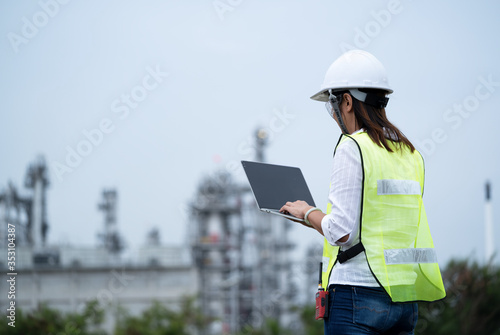 Engineer woman with laptop.Engineer woman wearing hard hat and reflective vest using laptop of power plant on background .