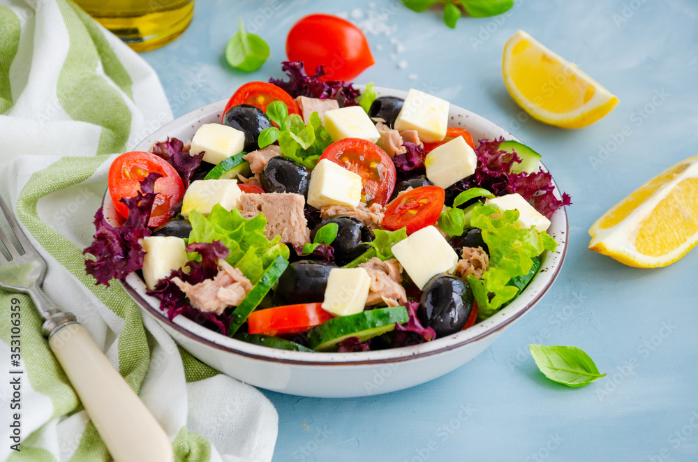 Salad with tuna, fresh vegetables, olives and feta cheese in a bowl on a light blue concrete background. Healthy food. Horizontal orientation.