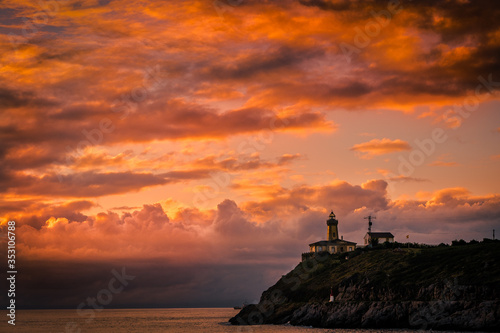 Hermoso atardecer sobre la ría con la silueta del faro sobre la montaña con colores cálidos en las nubes 