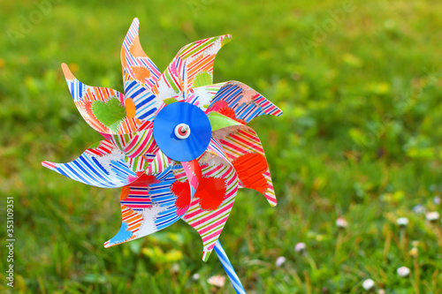 Children's colorful plastic toy windmill  turbine on green blurred grass background outdoors in sunny summer day.  © Inga