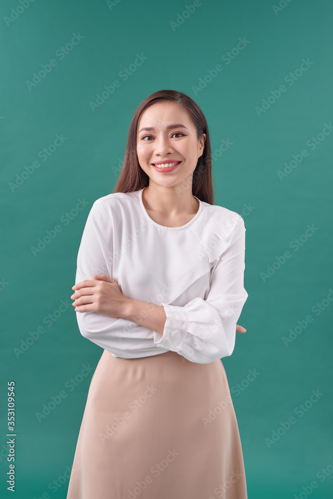 portrait of pretty asian girl smiling with arm crossed on turquoise background