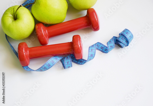 The concept of diet, vegetables and dumbbells and scales on a wooden background