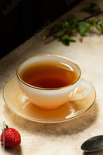 cup of black tea on beige background close up. with strawberry and spoon as decor. vertical