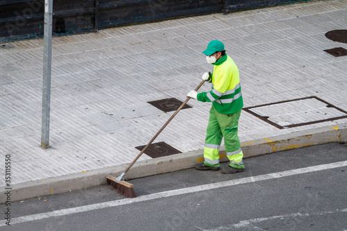 Street sweeper wearing face mask working on a sidewalk. Public cleaning concept during coronavirus pandemic