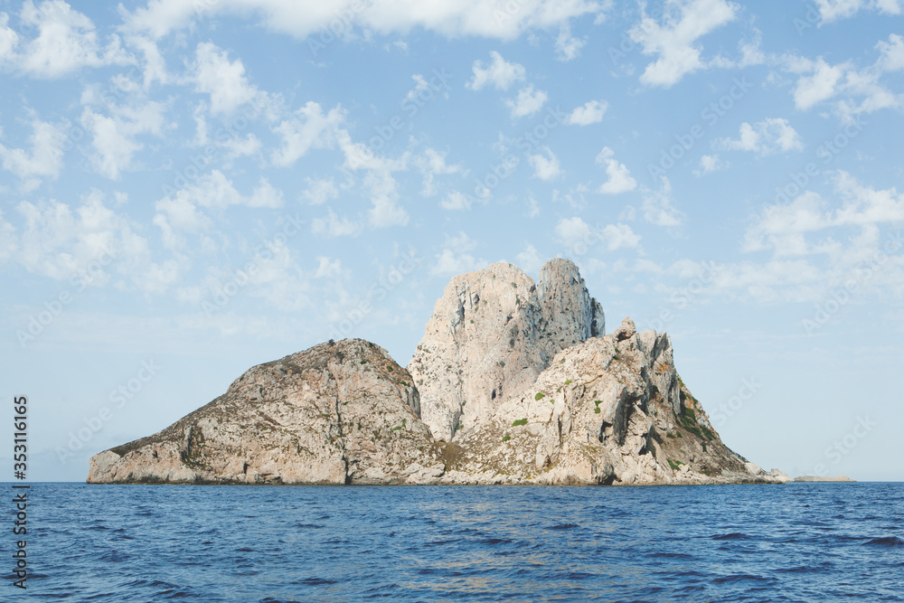 Beautiful image with clouds in the sky, waves and a small islet of the mediterranean.