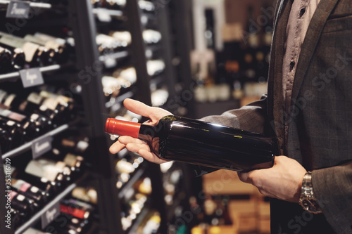 Bartender sommelier takes bottle of red wine from counter of restaurant drinks store
