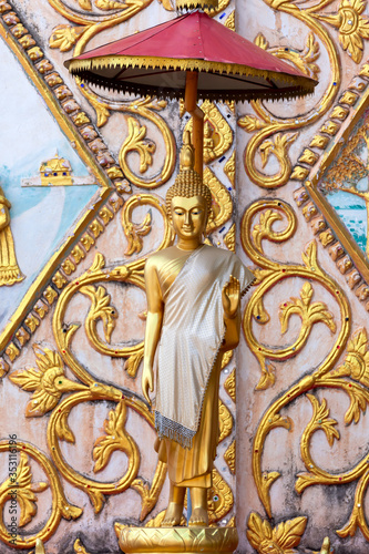 Vertical image Statue of gold Buddha leela standing with Stucco Laos style on the wall