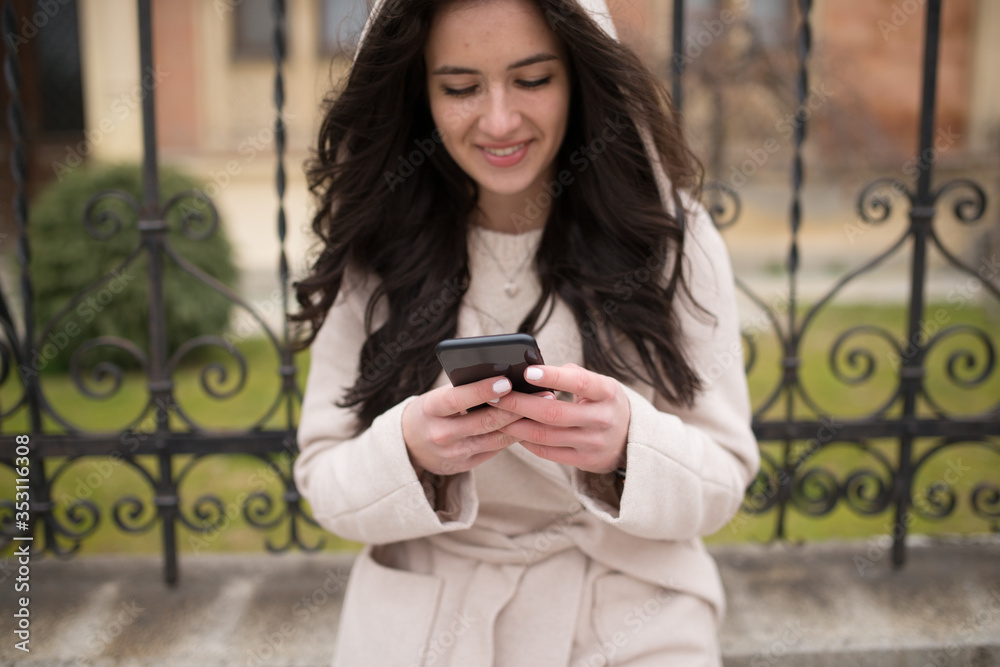 smiling black haired girl who is on the streets and uses a mobile phone