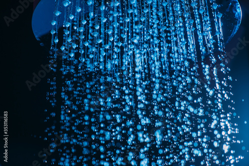 Drops of water fall from a watering can in the shower in blue light. Water drops close-up. Flow of water. Big round watering can macro photo..
