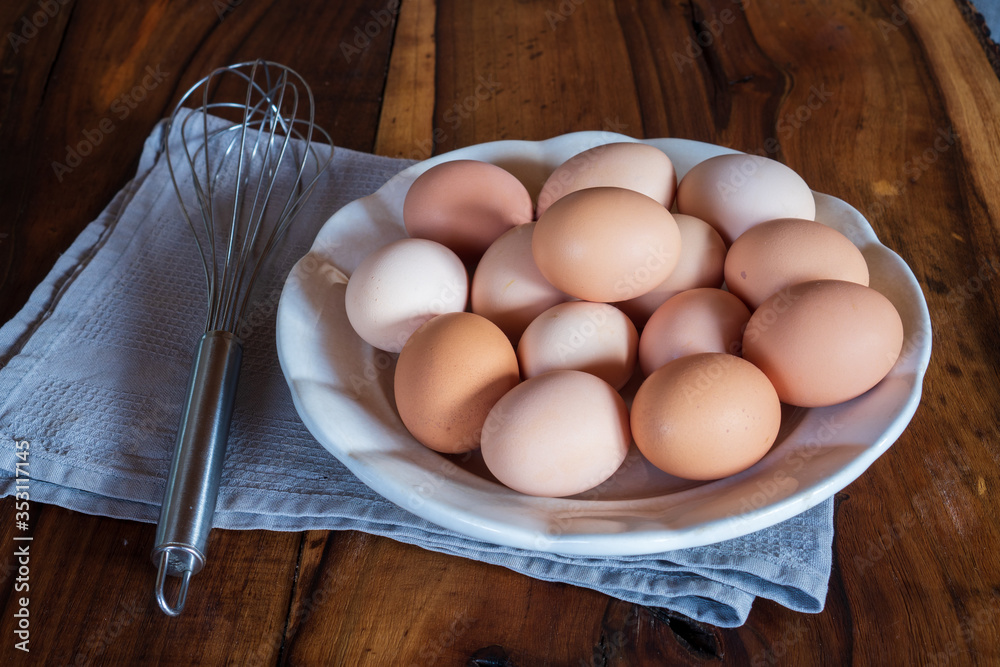 Raw chicken eggs on white plate with whisk on wooden background. Ready to start the cooking concept Raw chicken eggs on white plate with whisk on wooden background. Ready to start the cooking concept