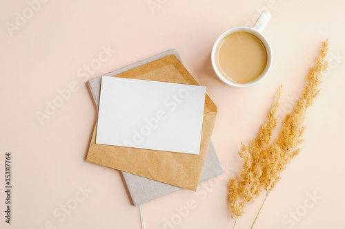 Flat lay composition with envelope, invitation card mockup, cup of coffee and dry flowers on beige background. Top view wedding invitation or love letter