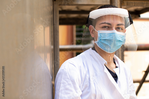 Tecnico specialista in camice bianco e schermo protettivo in plexiglass indossa mascherina chirurgica  in contesto industriale. photo