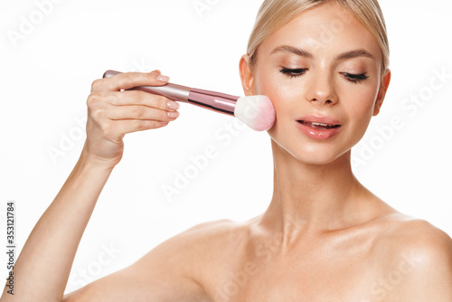 Image of shirtless woman using powder brush and looking at camera