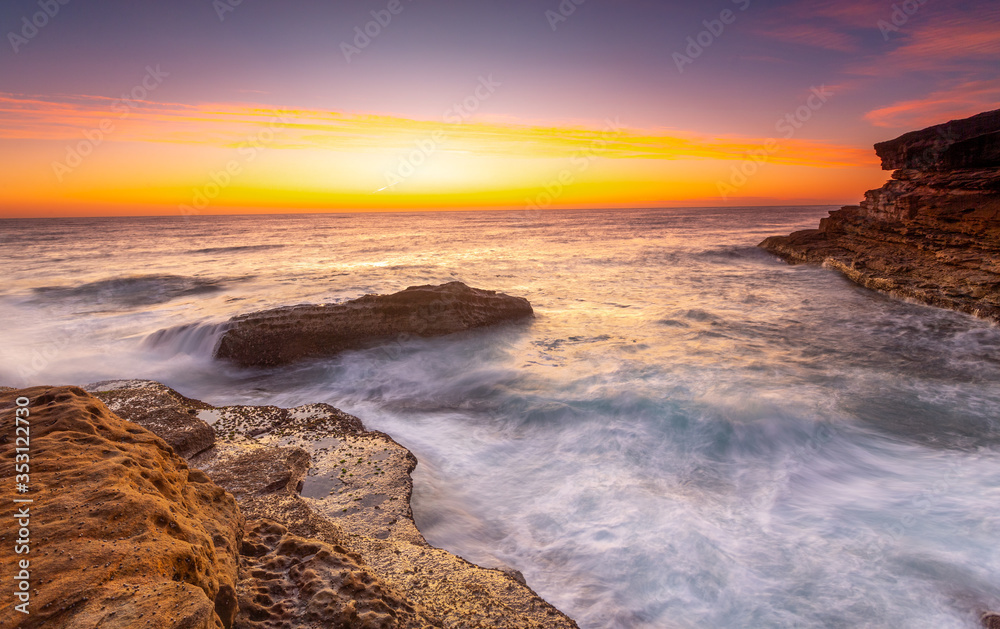 Fototapeta premium Sunrise over the ccean with some foreground rocks of eroded sandstone