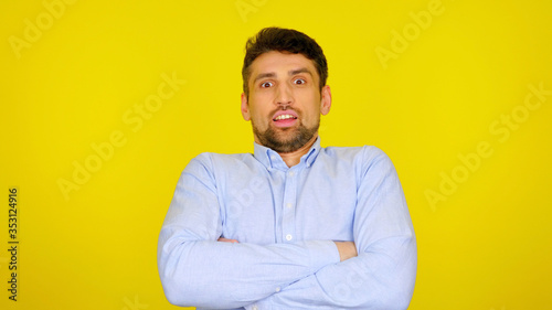 Bearded man with hands on his chest is shocked by what he saw. Surprised guy in a light blue shirt on a yellow background with copyspace. Place for text or product