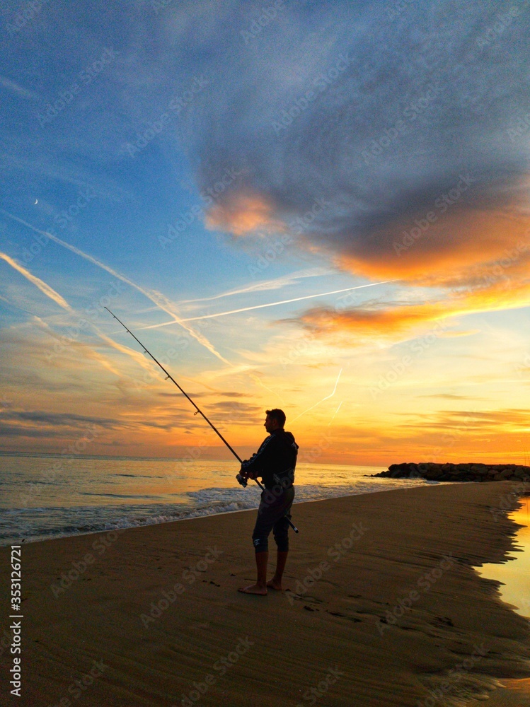 man fishing at sunset on the shore of the beach, surfcasting