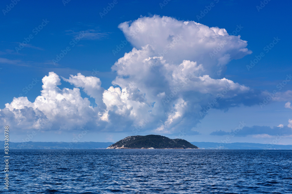 Landscape with the sea, island and beautiful clouds in the blue sky. Kelifos island, Aegean Sea, Halkidiki, Greece, view from the sea.