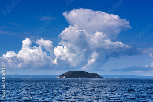 Landscape with the sea, island and beautiful clouds in the blue sky. Kelifos island, Aegean Sea, Halkidiki, Greece, view from the sea.