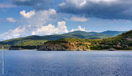 View of the shore from the sea. Landscape with the sea and beautiful clouds in the blue sky. Sithonia, Halkidiki, Greece.