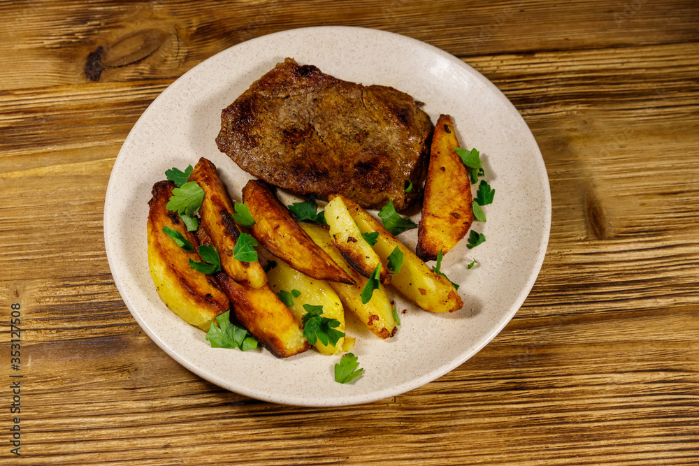 Fried beef steak with potato wedges on wooden table Fried beef steak with potato wedges on wooden table