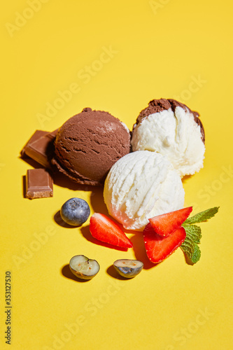 tasty brown and white ice cream with berries, chocolate and mint on yellow background