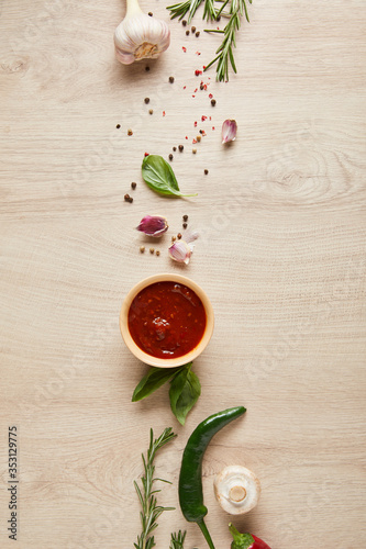 Fototapeta Naklejka Na Ścianę i Meble -  top view of delicious tomato sauce in bowl near herbs and spices on wooden table