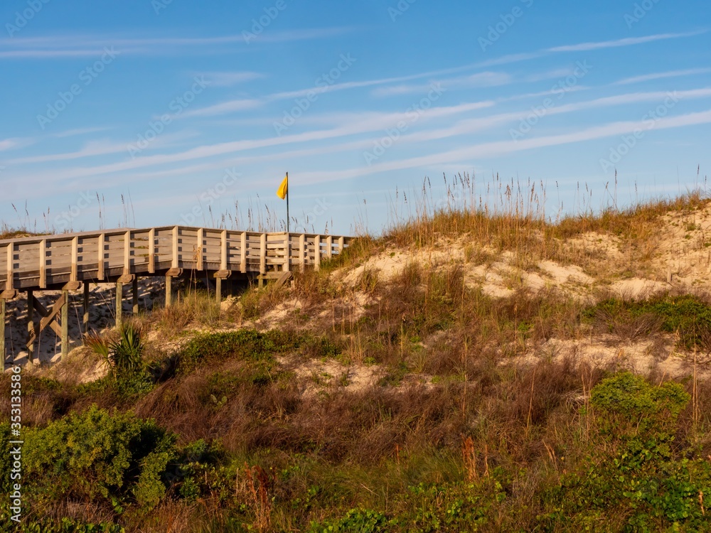 Anastasia State Park in St. Augustine, Florida at golden hour, with a wooden boardwalk and sand dune with a pretty blue sky.  Nature landscapes near the ocean.