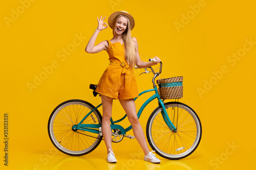 Cute girl in summer jumpsuit, hat and sunglasses posing with vintage bicycle