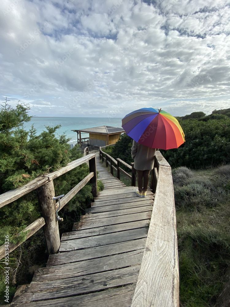 Woman with colorful umbrella walk in wooden pathway and watching a winter sea panorama