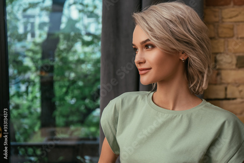 smiling, attractive woman looking away while standing near window at home
