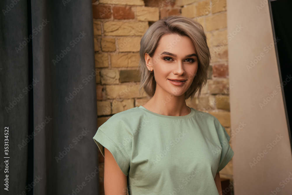 attractive woman smiling at camera while standing near brick wall at home attractive woman smiling at camera while standing near brick wall at home
