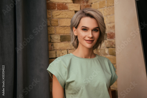 attractive woman smiling at camera while standing near brick wall at home