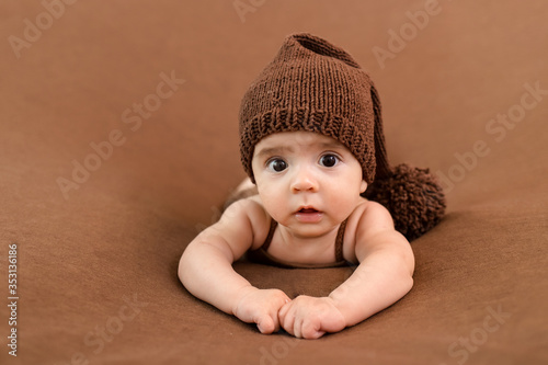 Cute newborn baby on a brown blanket. Smiling baby on a dark background. Closeup portrait of newborn baby. Baby goods packing template. Nursery. Medical and healthy concept. 