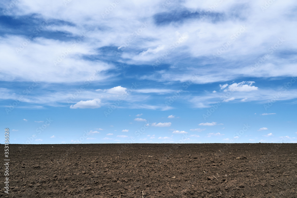 plowed field, soil and clouds of a bright sunny day - concept of agriculture