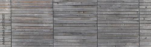 Long gray wooden fence in a panoramic view. Horizontal wood panels with knotes in three blocks. For abstract wooden backgrounds and textures.
