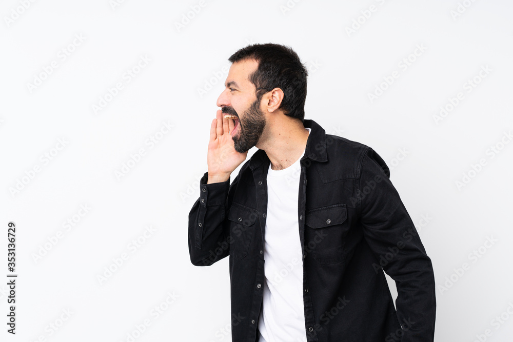 Young man with beard over isolated white background shouting with mouth wide open to the lateral Young man with beard over isolated white background shouting with mouth wide open to the lateral