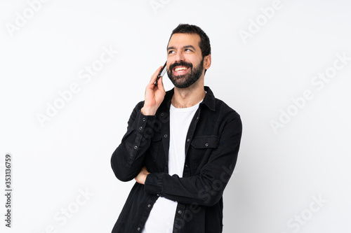 Young man with beard over isolated white background keeping a conversation with the mobile phone