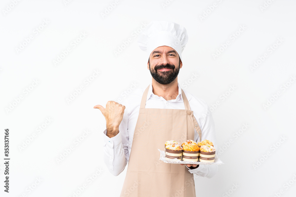 Young man holding muffin cake over isolated white background pointing to the side to present a product Young man holding muffin cake over isolated white background pointing to the side to present a product