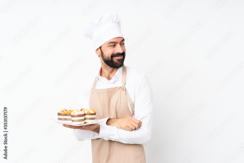 Young man holding muffin cake over isolated white background with arms crossed and happy Young man holding muffin cake over isolated white background with arms crossed and happy