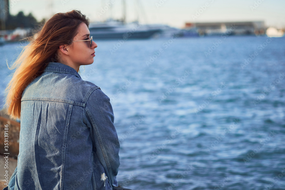 view from the back a beautiful girl in sunglasses sits and looks to the right against the background of the sea