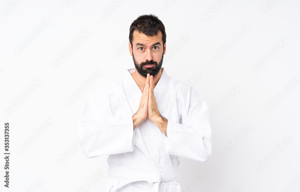 Young man doing karate over isolated white background keeps palm together. Person asks for something Young man doing karate over isolated white background keeps palm together. Person asks for something