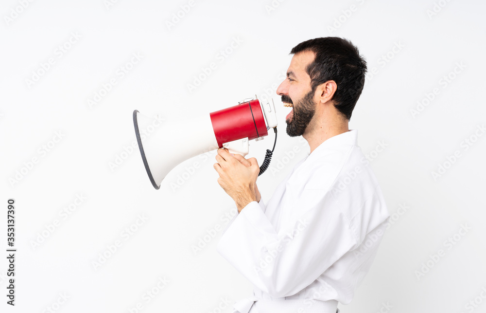 Young man doing karate over isolated white background shouting through a megaphone Young man doing karate over isolated white background shouting through a megaphone