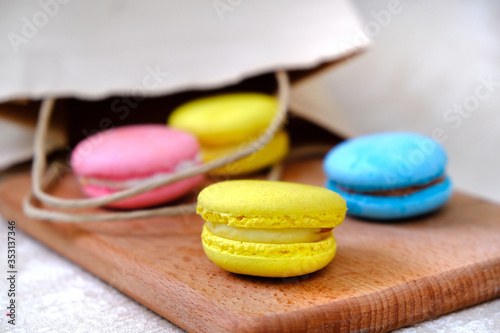 Colorful french Sweet Cakes Macaroons from paper bag onto wooden plate.